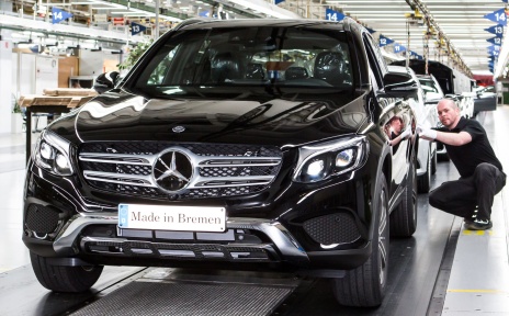 Ein Mann kniet neben einem neu produzierten dunklen Mercedes.